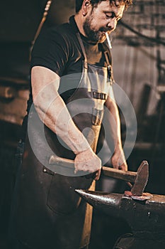 Senior blacksmith forging molten metal on the anvil in smithy.