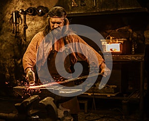 Senior blacksmith forging the molten metal on the anvil in smithy