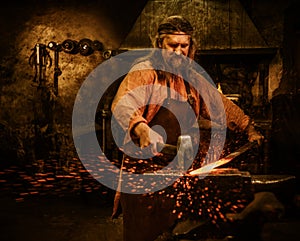 Senior blacksmith forging the molten metal on the anvil in smithy