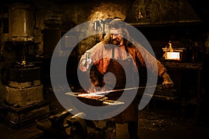 Senior blacksmith forging the molten metal on the anvil in smithy