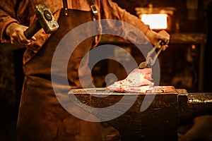 Senior blacksmith forging the molten metal on the anvil in smithy