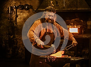 Senior blacksmith forging the molten metal on the anvil in smithy