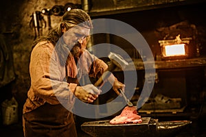 Senior blacksmith forging the molten metal on the anvil in smithy