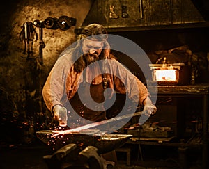 Senior blacksmith forging the molten metal on the anvil in smithy