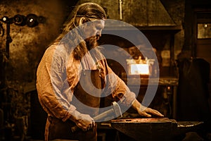 Senior blacksmith forging the molten metal on the anvil in smithy