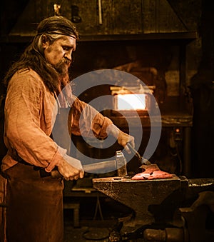 Senior blacksmith forging the molten metal on the anvil in smithy