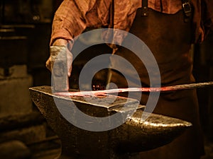 Senior blacksmith forging the molten metal on the anvil in smithy