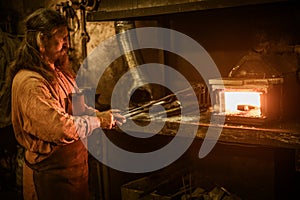 Senior blacksmith heats item before forgingin smithy