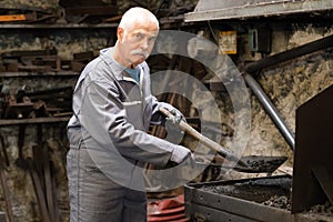 Senior blacksmith heats item before forgingin smithy