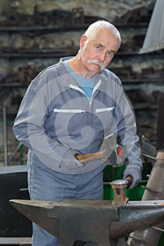Senior blacksmith working metal with hammer
