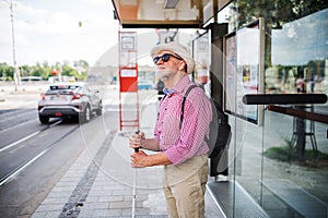 Senior blind man with white cane waiting at bus stop in city.