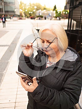 senior blonde business woman looks at cell phone holding glasses photo