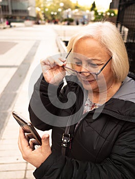 senior blonde business woman looks at cell phone holding glasses photo