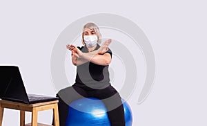 Senior blonde woman, fitness coach in medical mask on quarantine gesturing stop sign with hands looking at laptop, sport