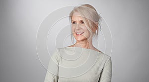 Senior blonde woman is toothy smiling looking away isolated