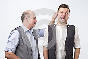 Senior boss pulling young man ear, punishing for mistake at work.