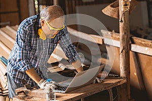 Senior builder wood worker using laptop computer at aiding design at construction work