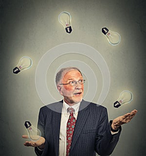 Senior business man executive in suit juggling playing with light bulbs