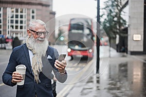 Senior business man going to work drinking coffee with london bus station in background - Focus on face