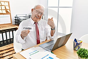 Senior business man holding fired banner at the office smiling happy and positive, thumb up doing excellent and approval sign