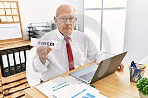 Senior business man holding fired banner at the office thinking attitude and sober expression looking self confident