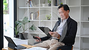 Senior business man holding smart phone and checking financial in modern office.