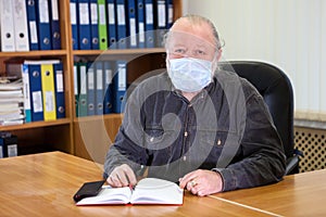 Senior business man wearing face mask sitting at the table in office room due Covid-19 flu