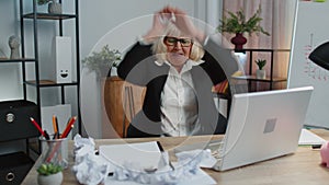 Senior business office woman use laptop throwing crumpled paper, having nervous breakdown at work