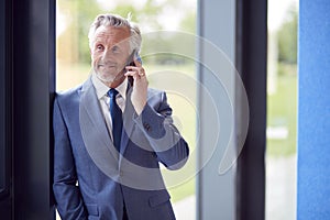Senior Businessman CEO Chairman By Window Inside Modern Office Building Calling On Mobile Phone