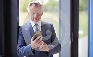 Senior Businessman CEO Chairman By Window Inside Modern Office Building Using Mobile Phone