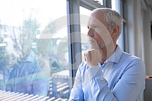 Senior businessman with hand on his chin looking through window at modern office