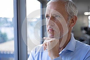 Senior businessman with hand on his chin looking through window at modern office