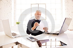 Senior businessman holding document in his hand while sitting at office desk and working