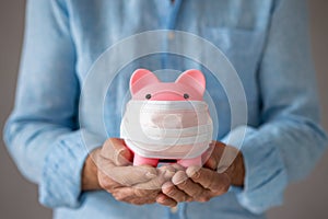 Senior businessman holding piggybank wearing protective medical mask