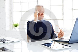 Senior businessman making a call while and using laptop while working in the office