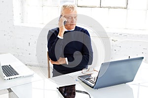 Senior businessman making a call while and using laptop while working in the office