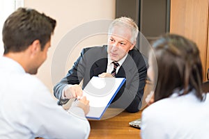 Senior businessman showing a document to sign to a couple: Document signature