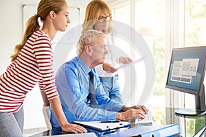 Senior businessman sitting in front of computer with his team. Teamwork.