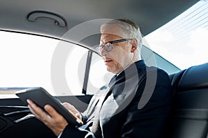 Senior businessman with tablet pc driving in car