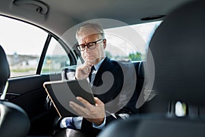 Senior businessman with tablet pc driving in car