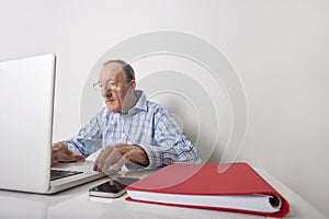 Senior businessman using laptop with book binder and cell phone on office desk