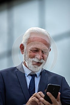 Senior businessman using mobile phone in front of office building