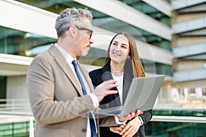 A senior businessman and a younger female colleague engage with content on a laptop together