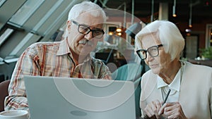 Senior businesspeople man and woman talking looking at laptop screen in cafe