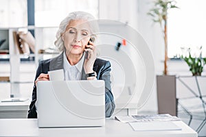 Senior businesswoman holding coffee cup and talking on smartphone