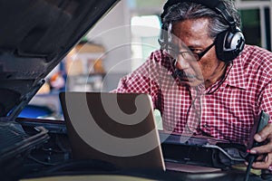 Senior car mechanic using ultrasonic sound system to check car engine performace at garage and car maintenance service station