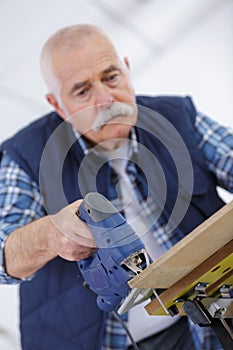 Senior carpenter drilling hole in wood plank in workshop