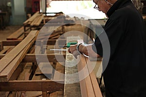 Senior carpenter measuring wooden plank in carpentry workshop.