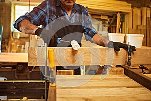 Senior carpenter in uniform gluing wooden bars with hand pressures at the carpentry