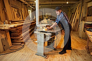 Senior carpenter in uniform works on a woodworking machine at the carpentry manufacturing
